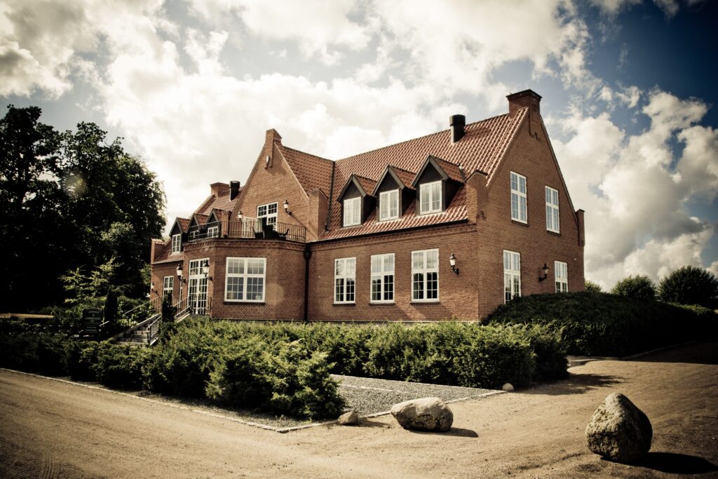 Elegant brick mansion with landscaped garden under a bright sunny sky.