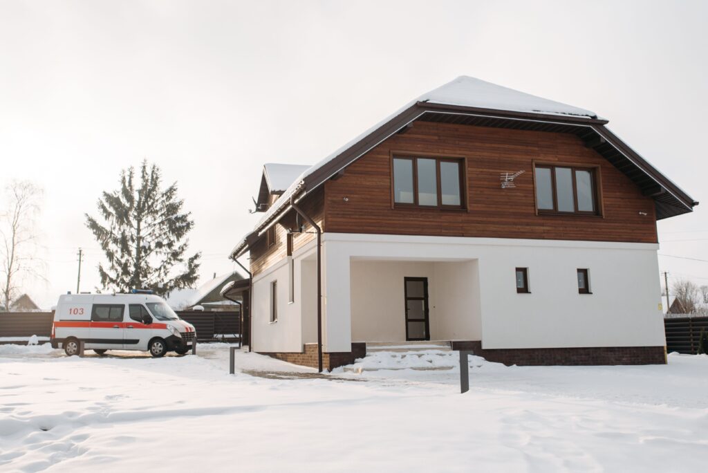 A suburban house with a snowy landscape and an ambulance parked nearby.